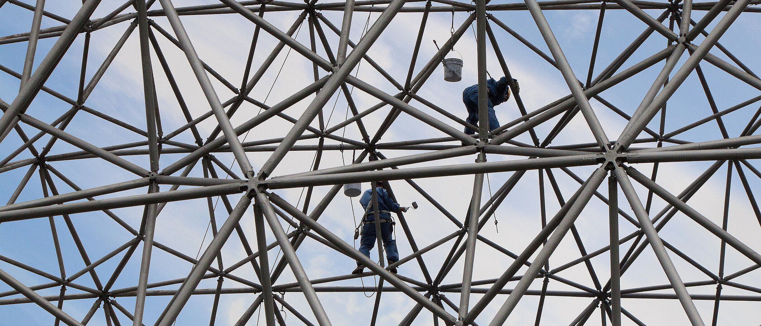 Climbers on a metallic net structure painting the sky.